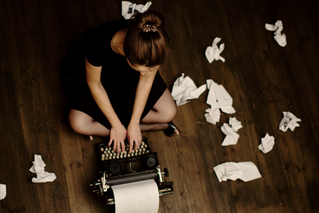 woman sitting on floor typing with papers scattered around her