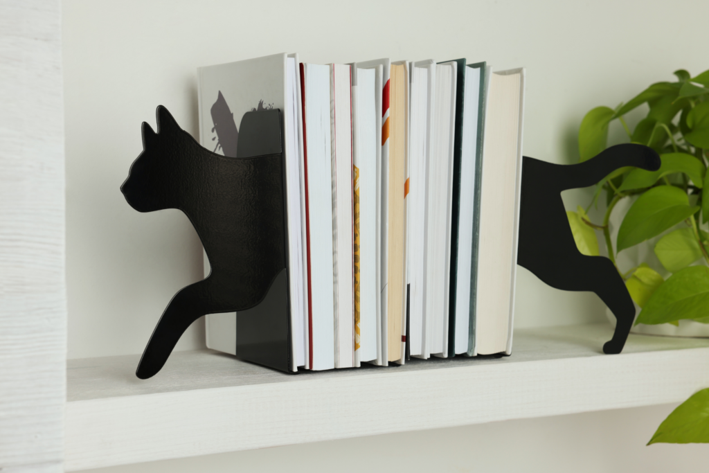 Books on a shelf with booksends that are both ends of a black cat